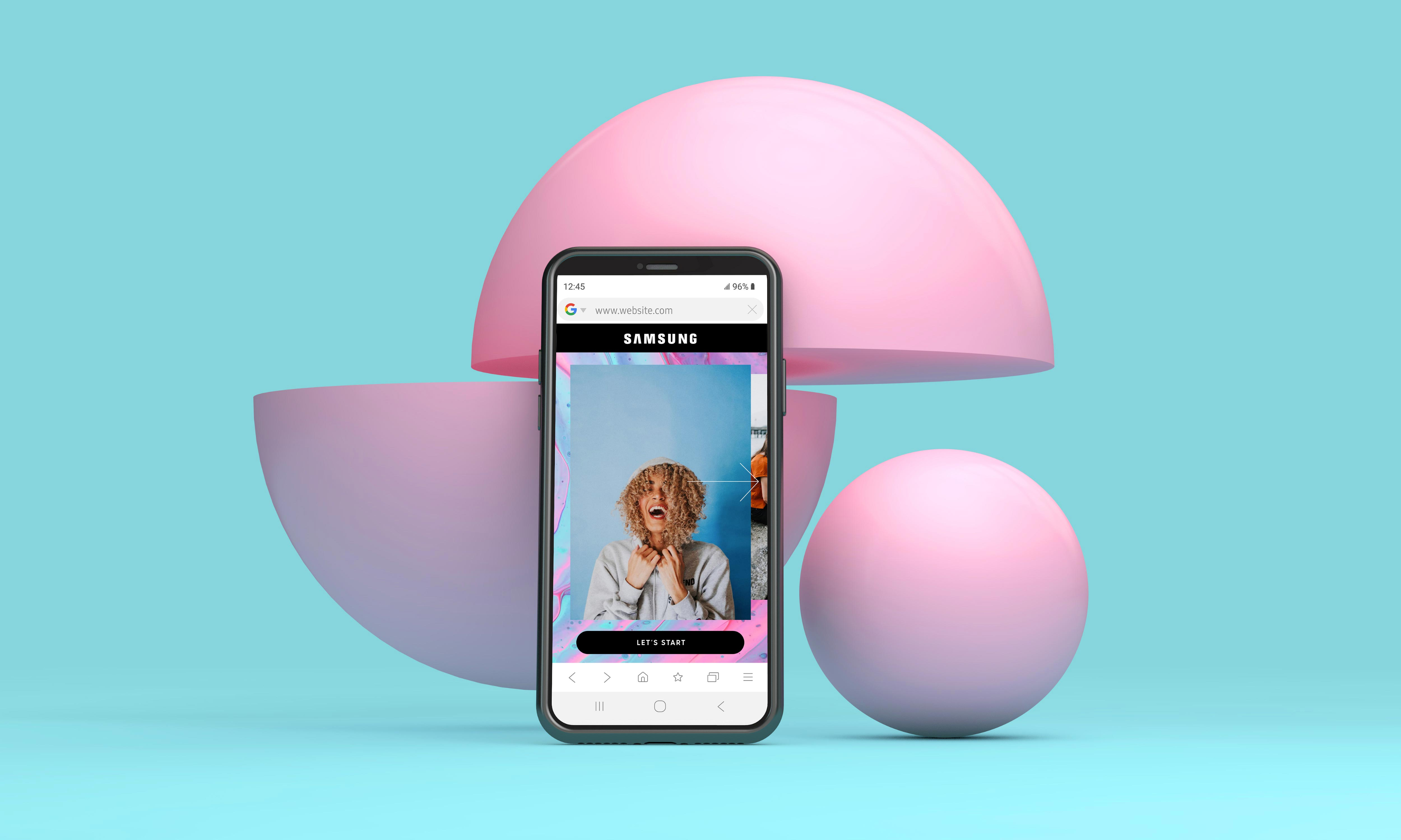 Smartphone displaying the Samsung mobile site with a woman on a pink backdrop, surrounded by pastel pink and blue spheres.
